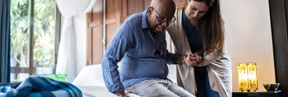 Caregiver and client sitting at a table in a sunny kitchen while client drinks a cup of coffee 