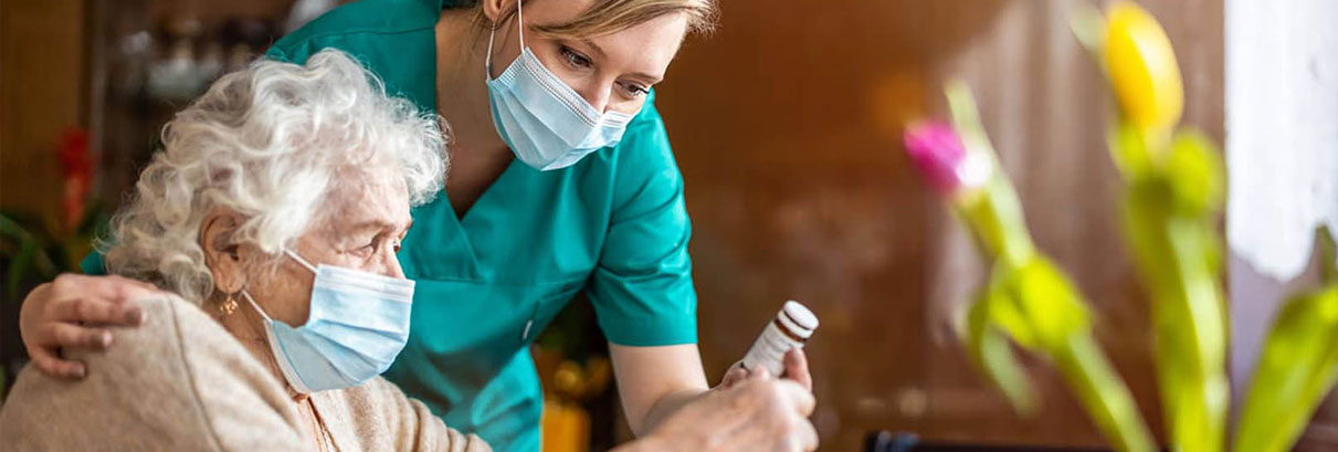 Caregiver and client sitting at a table in a sunny kitchen while client drinks a cup of coffee 