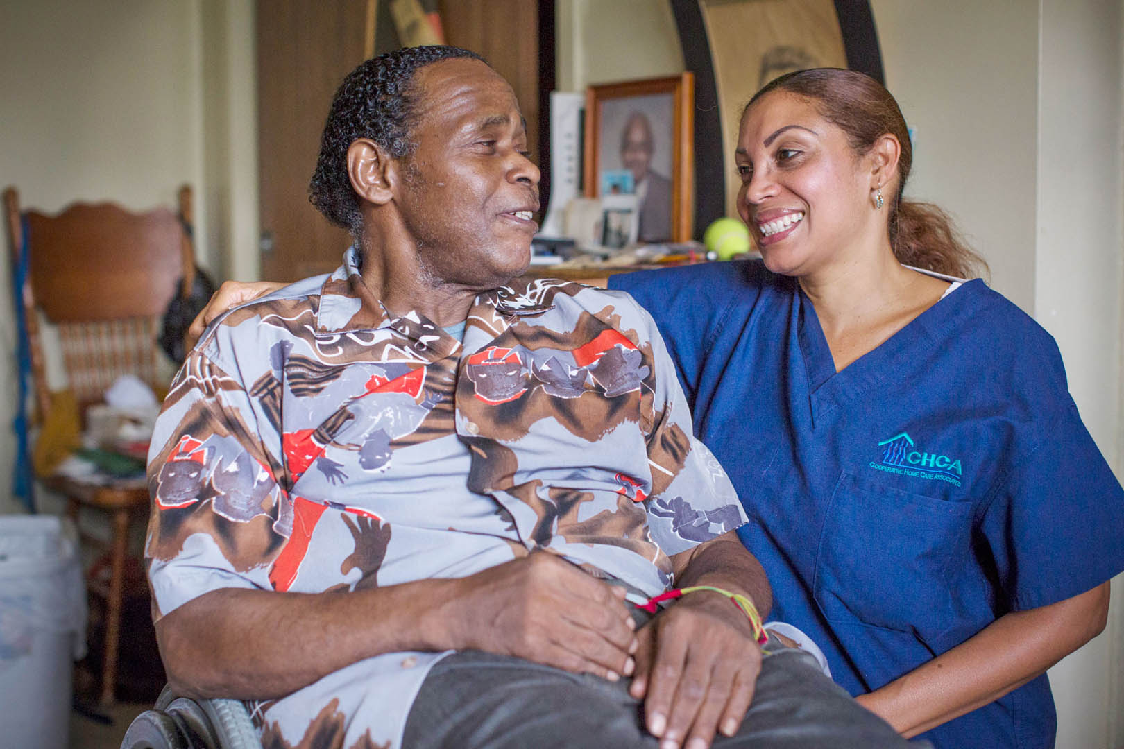 CHCA caregiver Rosa sits with client Floyd in his living room. They are looking at eachother and smiling
